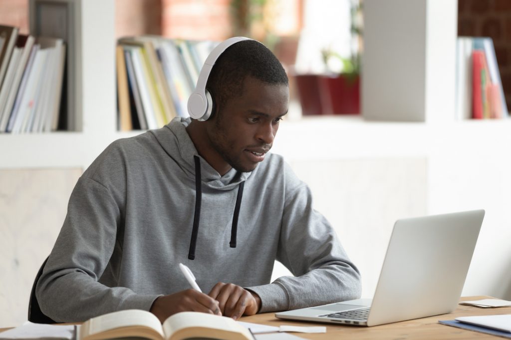 Homem estudando sozinho sentado ao computador e fazendo anotações. Estudar inglês