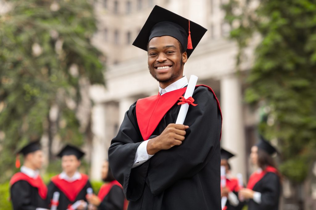 Homem trajando vestimenta de graduação e segurando um diploma