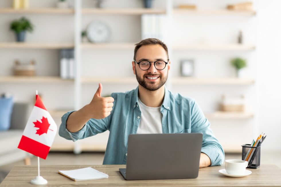 Homem sentado à mesa com computador e bandeira do Canadá