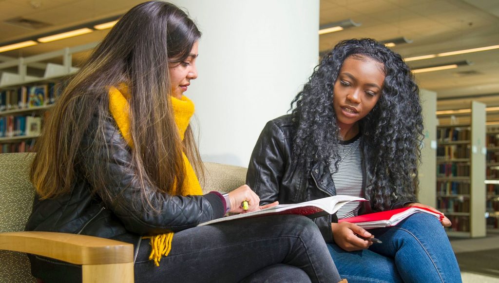 Duas estudantes conversando numa biblioteca