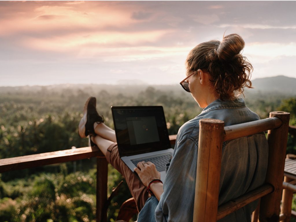 Aluna estudando no computador numa varanda com vista para um ambiente arborizado