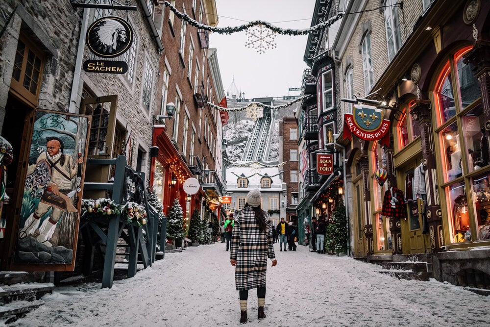 Rua de Quebec no inverno, cheia de neve, com uma visitante passeando | Viajar sozinha