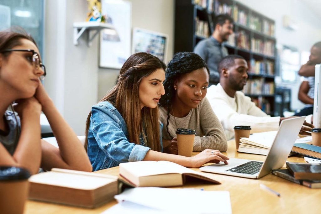 Duas estudantes conversando e resolvendo algo ao computador | Intercâmbio de estudo e trabalho